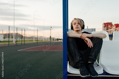 Young guy in headphones sitting on sports ground
