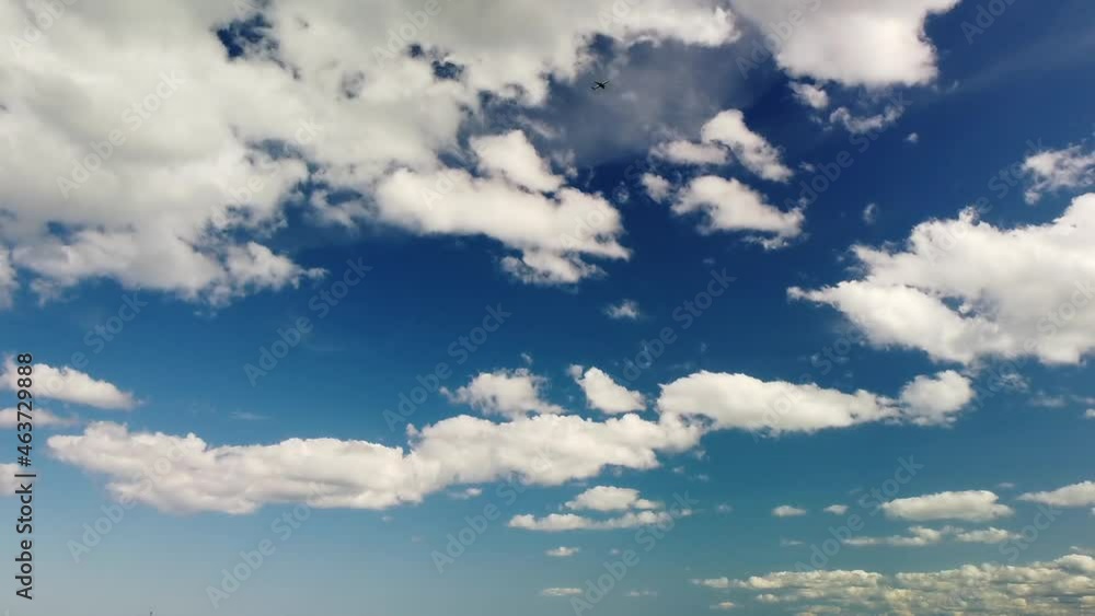 Clouds pass by a blue sky while an airplane ascends in the distance. Clouds pass by a blue sky while an airplane ascends in the distance.
