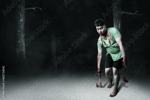 Fototapeta Naklejka Na Ścianę i Meble -  Scary zombie with blood and wound on his body holding ax and sickle walking