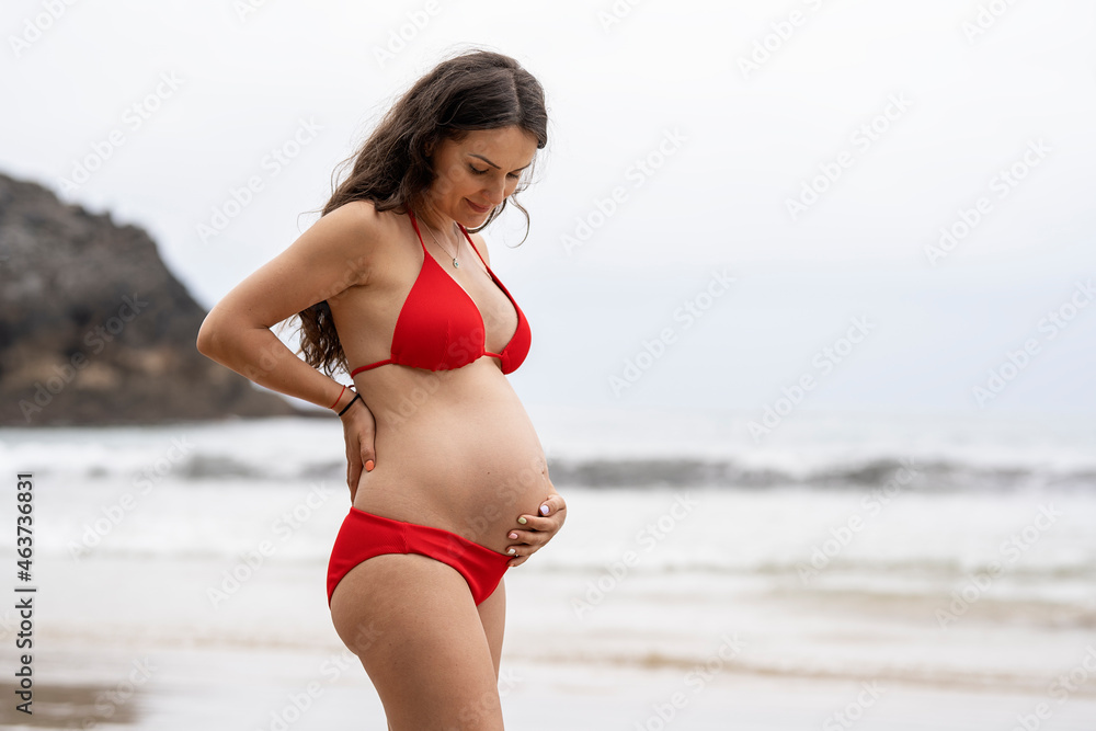 Pregnant woman touching and holding her belly while posing on th Pregnant woman touching and holding her belly while posing on th