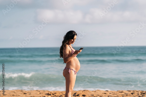 Pregnant woman using her mobile phone while standing on the beac photo