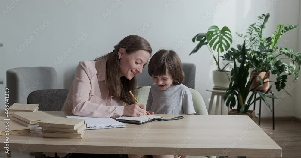 Attentive, funny toddler child diligently learning how to write and draw with his caring mother at home. Nanny teacher helping the preschooler develop artistic abilities and improve skills for school. Attentive, funny toddler child diligently learning how to write and draw with his caring mother at home. Nanny teacher helping the preschooler develop artistic abilities and improve skills for school.