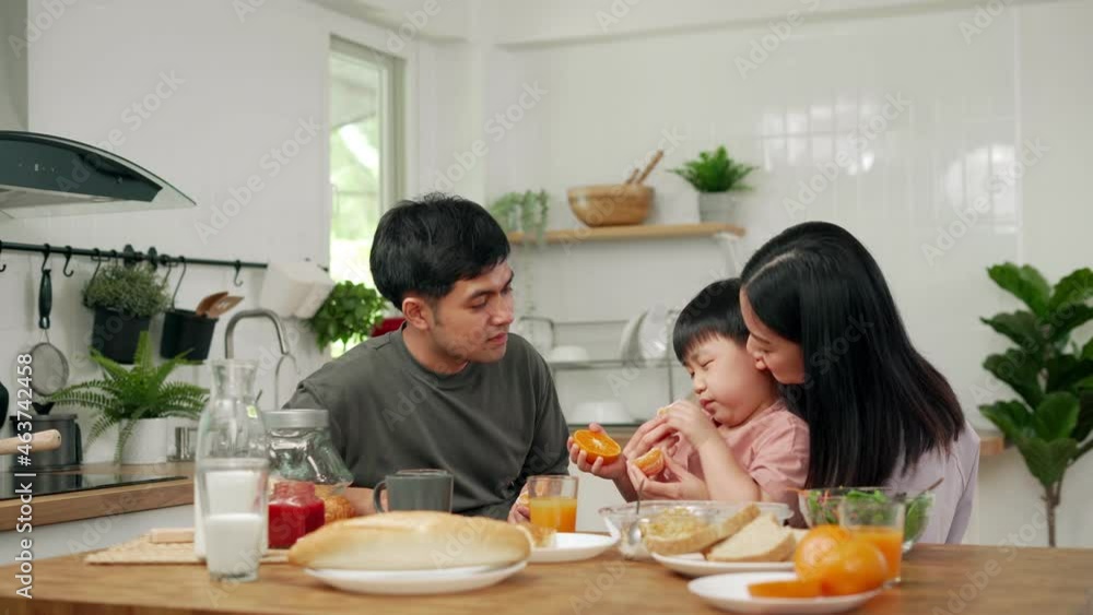 Happiness and smiles in the family. Asian parents and children eat breakfast together during the holidays. Mother feeds her children oranges for fun. Happiness and smiles in the family. Asian parents and children eat breakfast together during the holidays. Mother feeds her children oranges for fun.