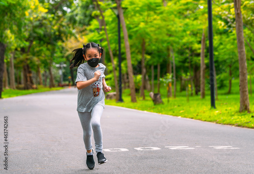 Asian child girl at 8 years old is running in the park, wearing protective medical mask, black long hair, front view, blank space for copy and design.