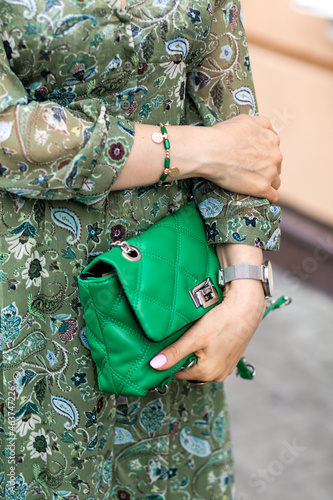 Young woman in a beautiful green dress with a print holds a fashionable green bag in her hands