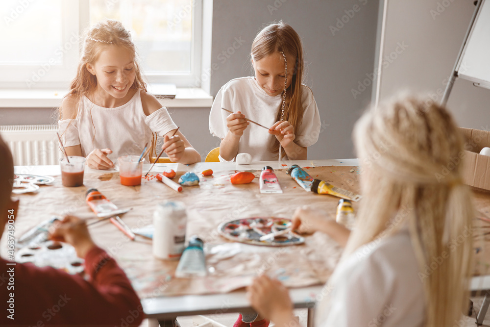 Happy children painting on paper with colorful paints in school Happy children painting on paper with colorful paints in school