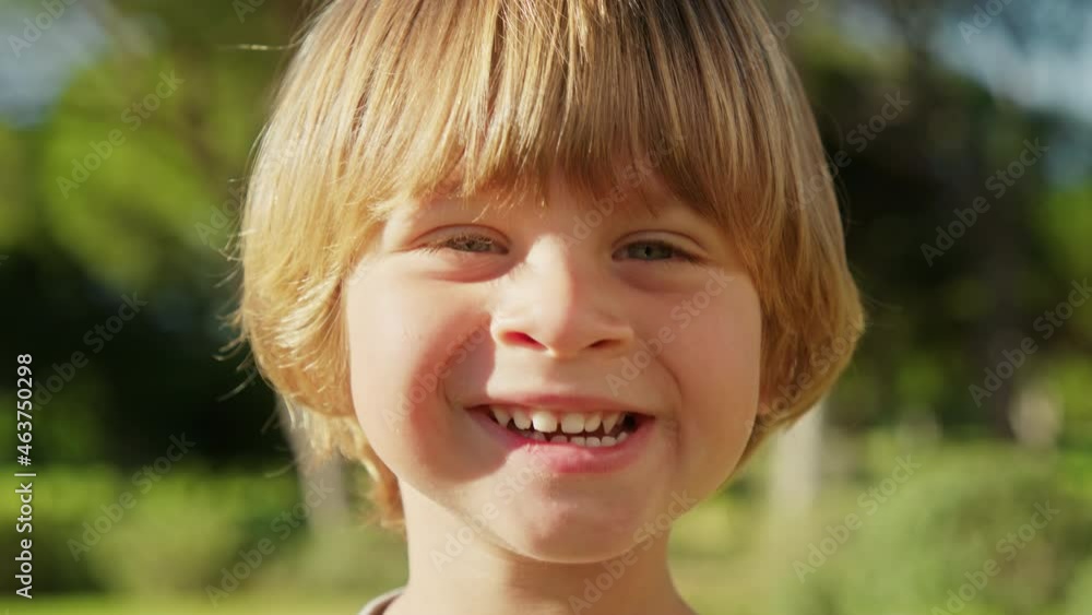 Close-up of a little blonde-haired kid within lush green garden and tall trees. Cute and playful child laughing lovely and cheerful, while having on weekend morning outdoor. High quality 4k footage Close-up of a little blonde-haired kid within lush green garden and tall trees. Cute and playful child laughing lovely and cheerful, while having on weekend morning outdoor. High quality 4k footage