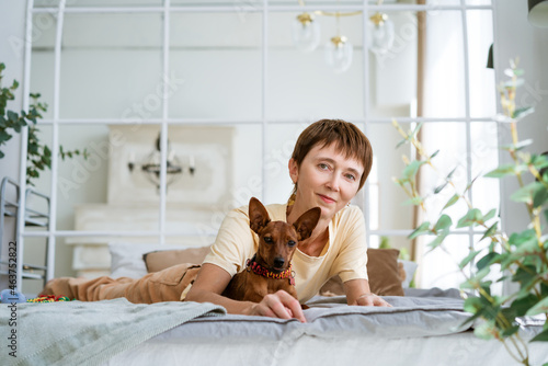 Cute woman lying on her stomach relaxing in bed with her beloved dog. Morning caresses in a warm comfortable bed. Cute woman and her dog are sleeping in bed,