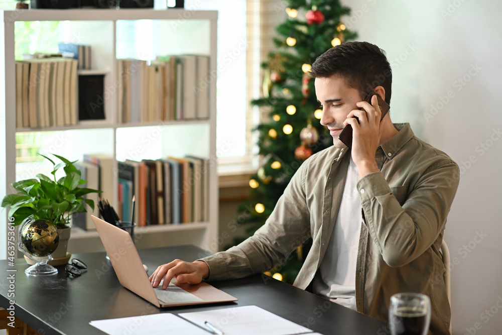 Man working with laptop computer and talking on mobile phone at home.