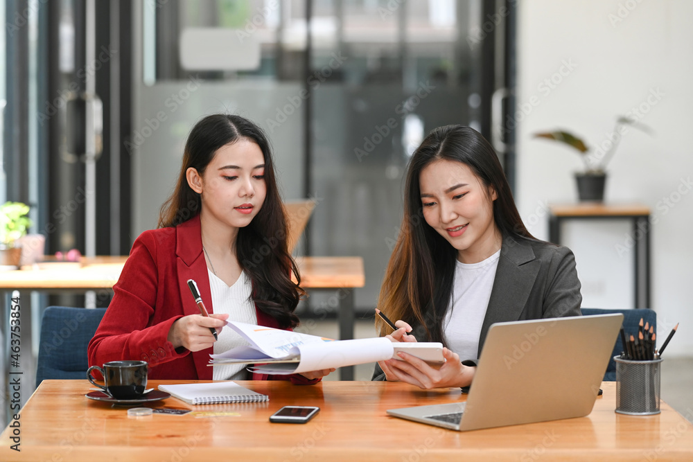 Two businesswoman colleagues sitting in office and analyzing financial documents together. Two businesswoman colleagues sitting in office and analyzing financial documents together.