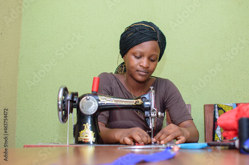 An African female tailor, fashion designer or dress maker, making stylish and fashionable clothes with sewing machine in a tailoring workshop