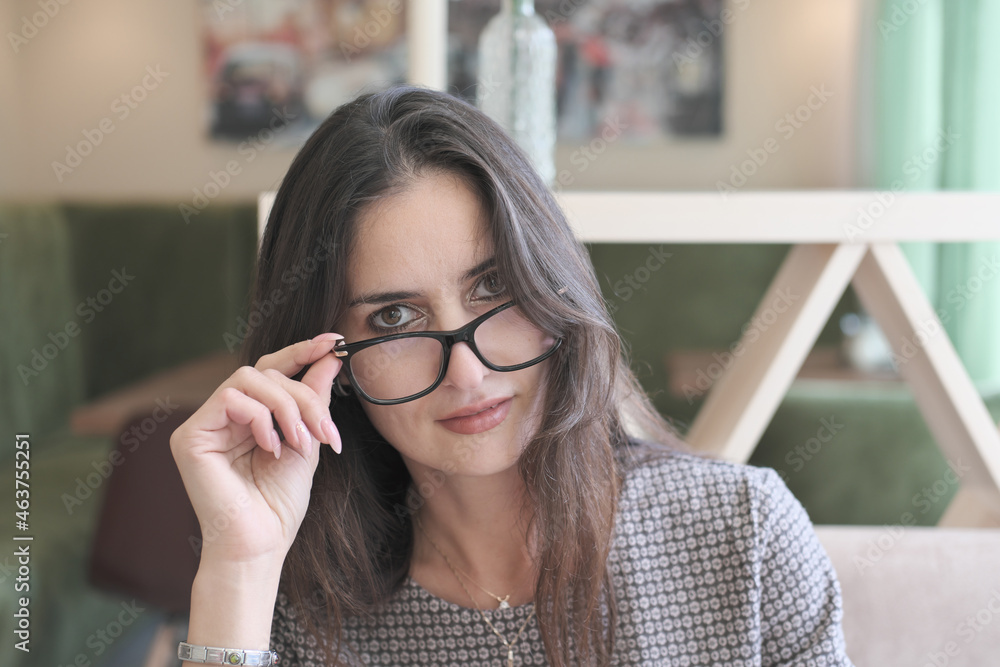 asian or middle east woman wearing eyeglasses looking at camera and touching her eyeglasses. getting rest or break in cafe, enjoying sunshine. beautiful happy smiling woman asian or middle east woman wearing eyeglasses looking at camera and touching her eyeglasses. getting rest or break in cafe, enjoying sunshine. beautiful happy smiling woman
