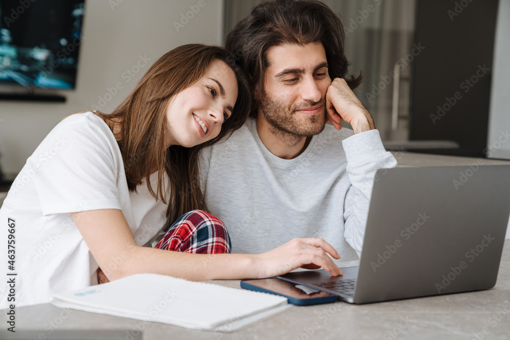 Young multiracial couple smiling while working with laptop together Young multiracial couple smiling while working with laptop together