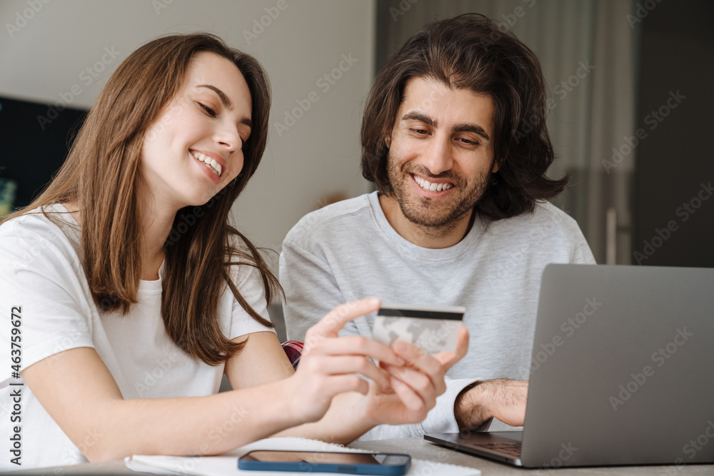 Young multiracial couple using credit card while working with laptop Young multiracial couple using credit card while working with laptop