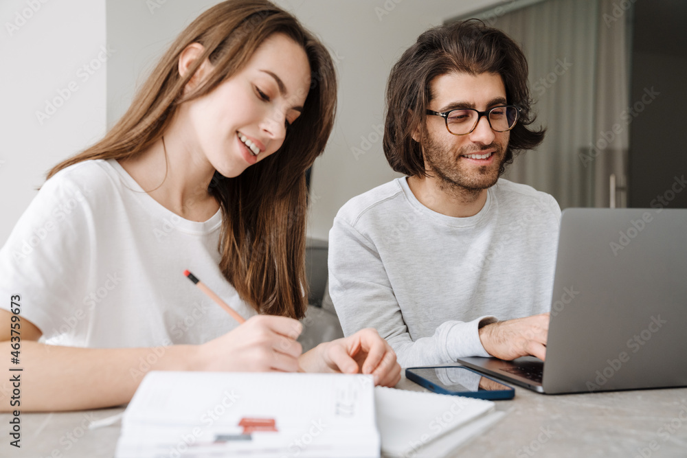 Young multiracial couple smiling while working with laptop together Young multiracial couple smiling while working with laptop together