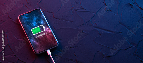 Mobile smart phone charge charging device on dark neon red and blue color background. Icon battery and charging progress lighting on screen.smartphones connected to power source.Low battery photo