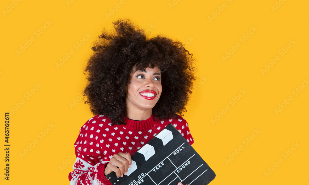 Exciting young woman holding a classic black paper board, isolated on a bright yellow background, studio portrait. Happy New Year concept of happy party