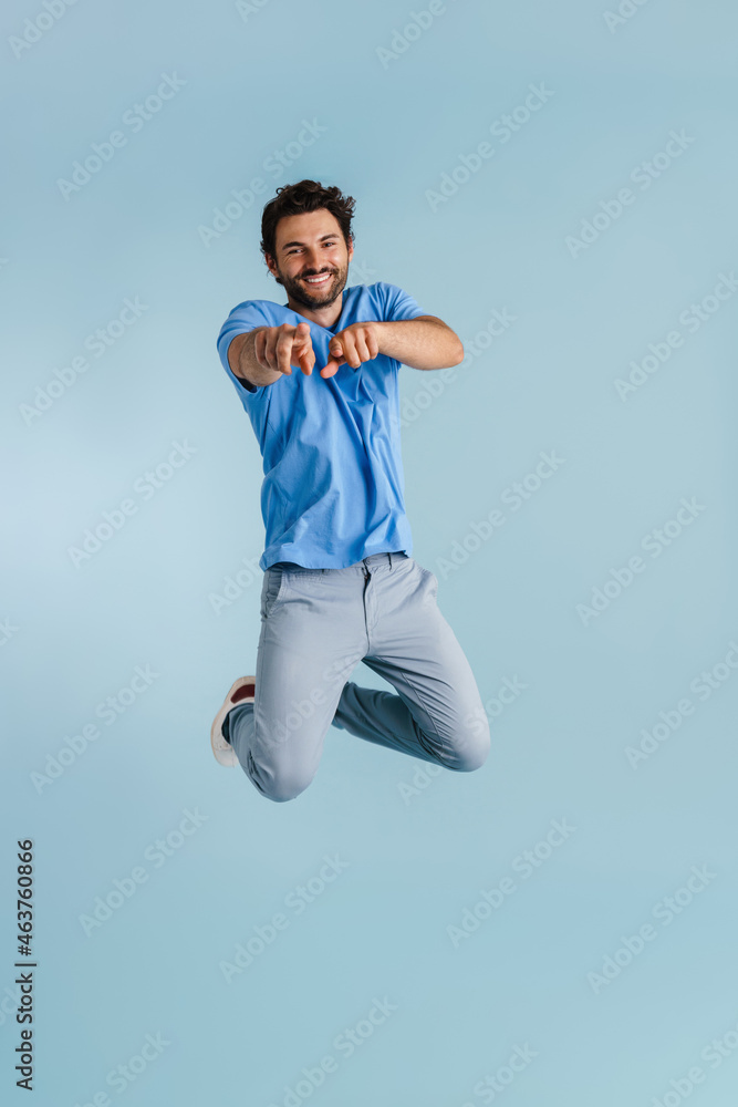 Young brunette man jumping while pointing fingers at camera