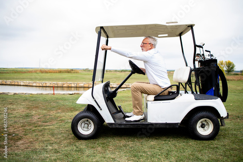 Senior man driving golf car to the green zone to continue playing golf.