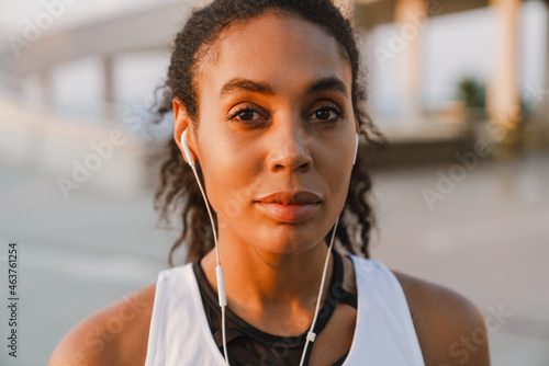 Black sportswoman listening music while working out on parking