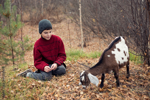 A boy in a red sweater and a little goat  in the forest.