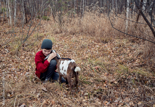 A boy in a red sweater and a little goat in the forest.