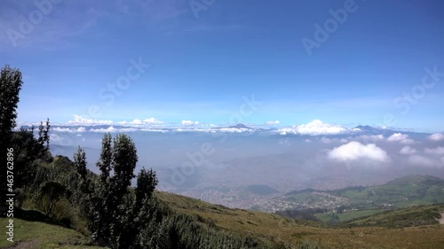 Panoramic view of the city of Quito, Ecuador, and the mountains and volcanoes that surround it. The sky is blue and there are some clouds above.
