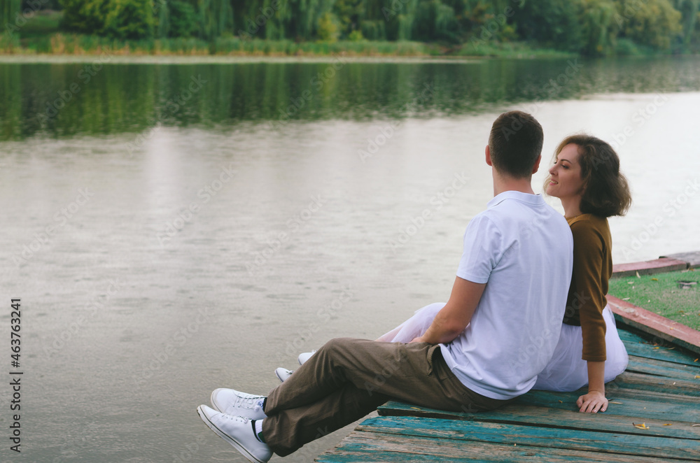 Love story of funny couple walking near river in hard rainfall with umbrella. cute man and woman in white skirt, yellow sweater. Family holiday and togetherness, date. Love story of funny couple walking near river in hard rainfall with umbrella. cute man and woman in white skirt, yellow sweater. Family holiday and togetherness, date.