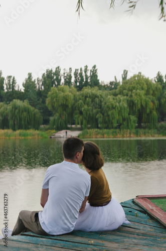 Love story of funny couple walking near river in hard rainfall with umbrella. cute man and woman in white skirt, yellow sweater. Family holiday and togetherness, date.