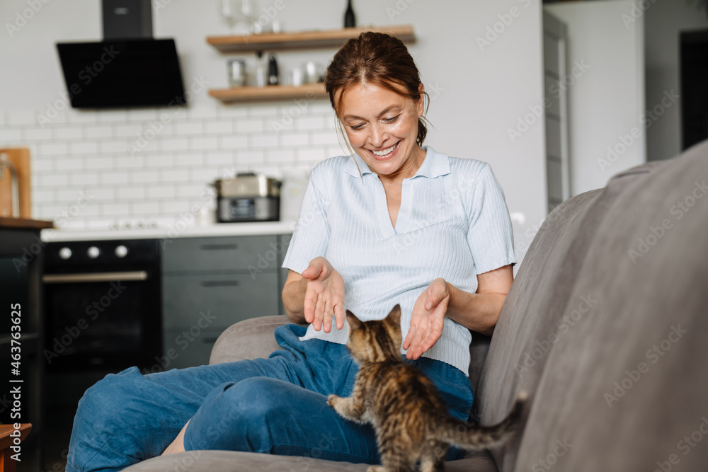 Ginger mature woman playing with her kitten while sitting on couch Ginger mature woman playing with her kitten while sitting on couch