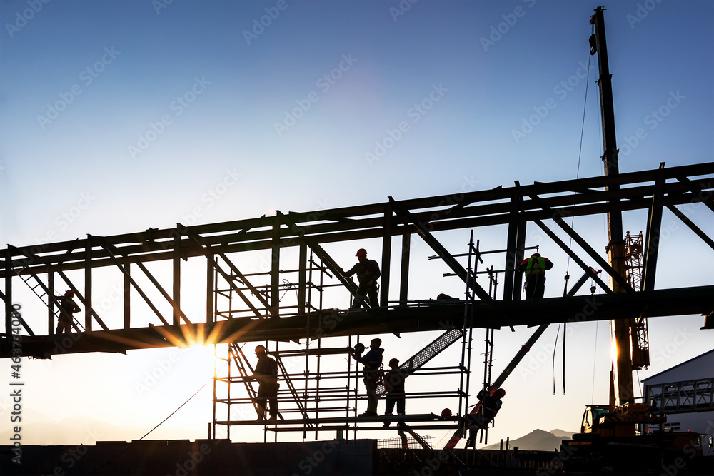 Construction workers are working on structure steel at sunset. A construction worker is a worker employed in manual labour of the physical construction of the built environment and its infrastructure. Construction workers are working on structure steel at sunset. A construction worker is a worker employed in manual labour of the physical construction of the built environment and its infrastructure.