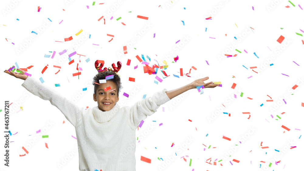Cheerful girl threw lot of confetti up. Child in white winter sweater, deer horns accessory, curly hair. Large multicolored confetti flying all over \ background. Holiday, Christmas party, fun concept Cheerful girl threw lot of confetti up. Child in white winter sweater, deer horns accessory, curly hair. Large multicolored confetti flying all over \ background. Holiday, Christmas party, fun concept