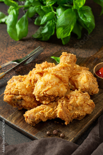 Fried crispy chicken legs in breadcrumbs on a wooden serving board on a dark background. Fast food from the drumstick close-up	