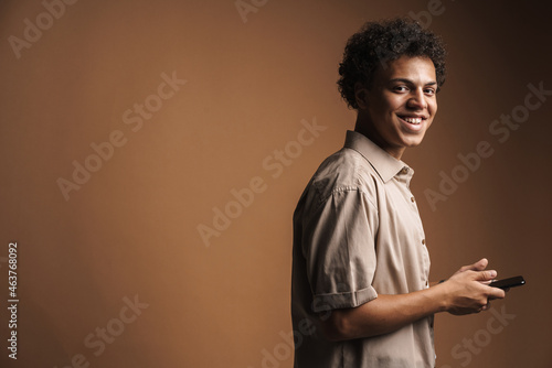 Young black man in shirt smiling while using mobile phone