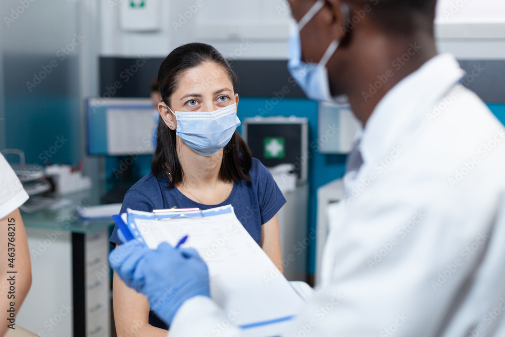 Closeup of african american pediatrician doctor writing ill expertise on clipboard explaining healthcare treatment to parent during clinical examination in hospital office. Therapist with face mask Closeup of african american pediatrician doctor writing ill expertise on clipboard explaining healthcare treatment to parent during clinical examination in hospital office. Therapist with face mask