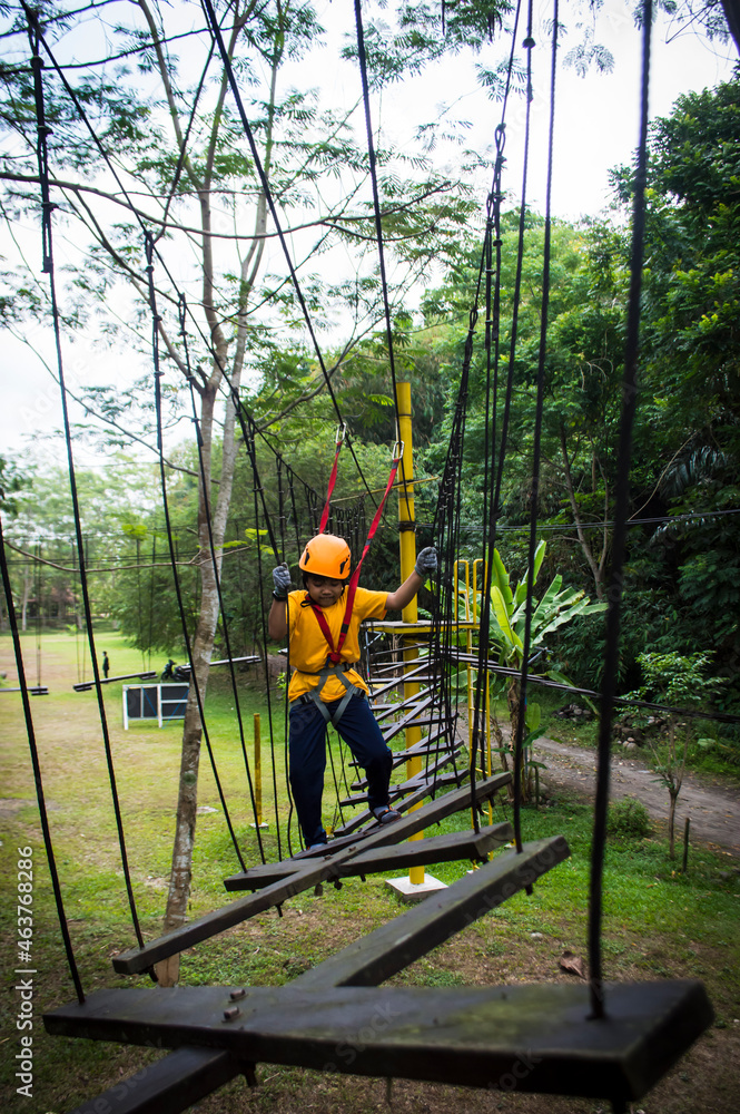 An Asian kid walking confidently and carefully through wooden boards hanged by safety ropes. An Asian kid walking confidently and carefully through wooden boards hanged by safety ropes.