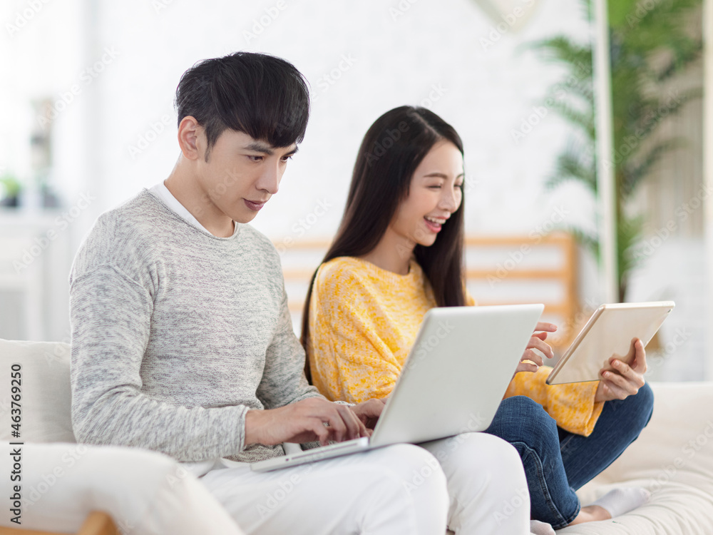 Young couple using laptop for office and watching movies on sofa at home Young couple using laptop for office and watching movies on sofa at home