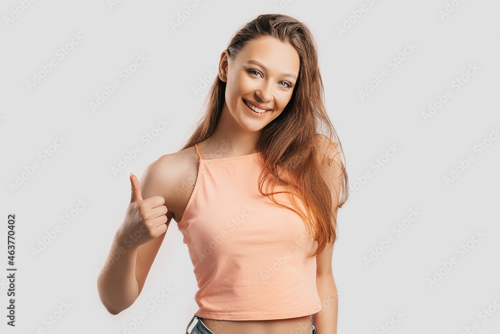 Beautiful young girl smiling and shows thumbs up gesture hand on a white isolated background. Positive woman points to an idea, a place for advertising Beautiful young girl smiling and shows thumbs up gesture hand on a white isolated background. Positive woman points to an idea, a place for advertising