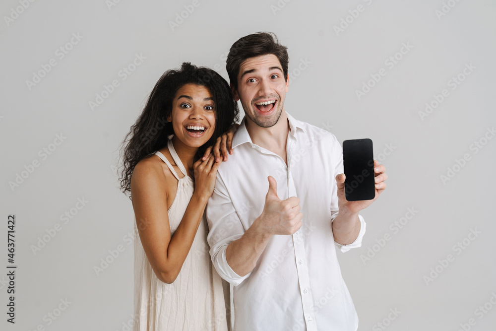 Multiracial excited man and woman gesturing and showing cellphone Multiracial excited man and woman gesturing and showing cellphone