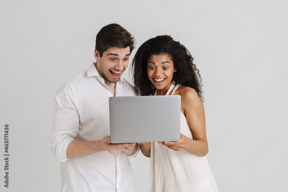 Multiracial excited couple posing with laptop and screaming Multiracial excited couple posing with laptop and screaming