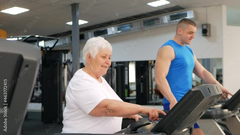 Happy smiling people are engaged in physical education, simulators in the gym. Active healthy lifestyle, senior concept. A woman with gray hair, a young coach is a muscular man. racecourse Happy smiling people are engaged in physical education, simulators in the gym. Active healthy lifestyle, senior concept. A woman with gray hair, a young coach is a muscular man. racecourse
