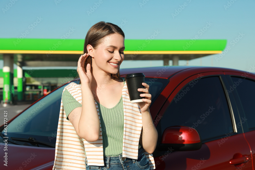 Beautiful young woman with coffee near car at gas station Beautiful young woman with coffee near car at gas station