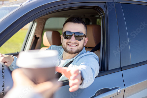 young smiling man driving car and taking away coffee. © Julija