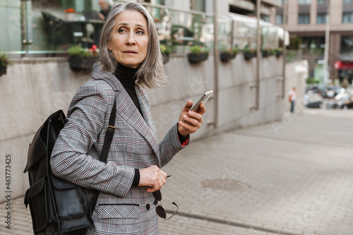 White senior woman using cellphone while standing at street