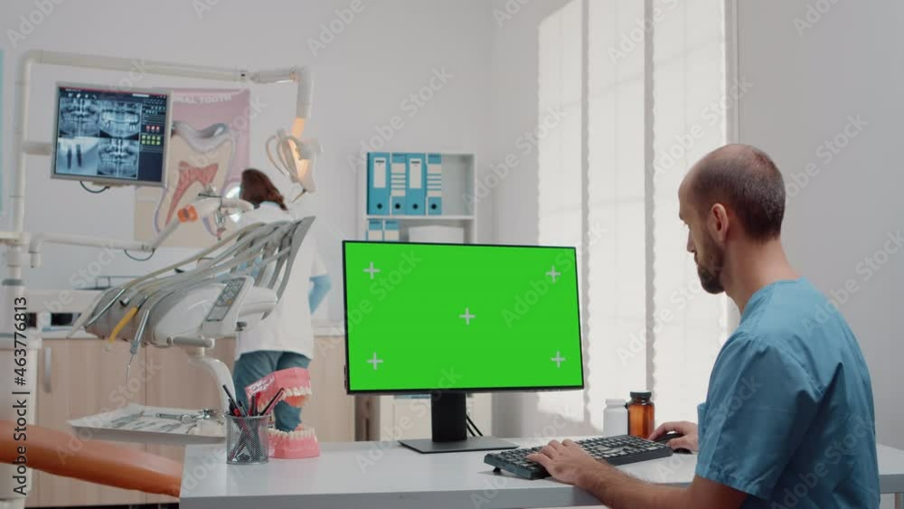 Man working with keyboard and computer with green screen on desk in dentistry office. Oral care assistant using mockup template and isolated background in dental cabinet for teethcare Man working with keyboard and computer with green screen on desk in dentistry office. Oral care assistant using mockup template and isolated background in dental cabinet for teethcare