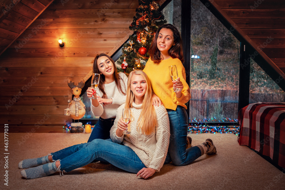 Christmas and new year. Three young happy women poses with glasses of champagne. Christmas tree on the background. Scandinavian style interior