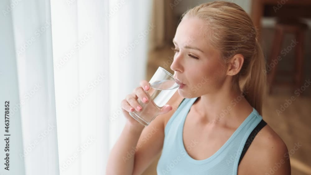 Overhead view of smiling woman drinking water and open a window in the morning Overhead view of smiling woman drinking water and open a window in the morning