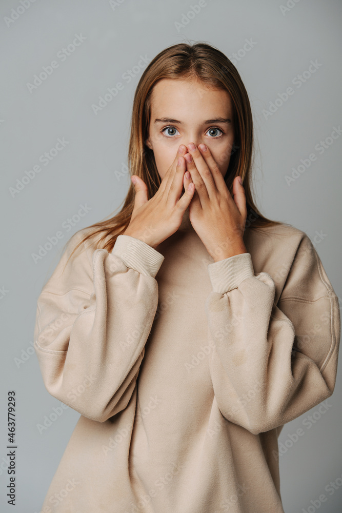 Surprised teenage girl covering her face with hands against grey background. Surprised teenage girl covering her face with hands against grey background.