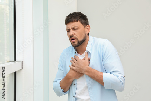 Man suffering from pain during breathing near window