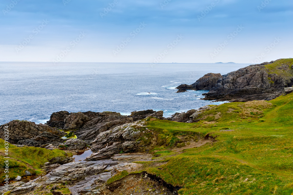 Rugged landscape at Malin Head, County Donegal, Ireland. Rough beach with cliffs, green rocky land with sheep on foggy cloudy day.